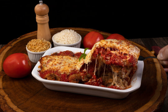 Steak Parmegiana or Parmegian Filet, made with breaded steak, tomato sauce, cheese au gratin. Accompanied by white rice and potato straw. Hand picking up piece with spatula to serve.