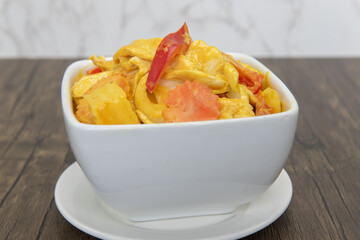 Spicy yellow curry presented perfectly in a bowl served upon a wooden plank table