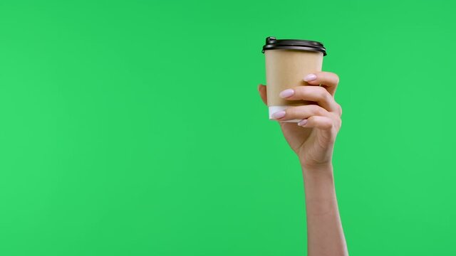 A woman's hand holds a paper cup of coffee, with the other hand points the index finger at the coffee and waves no, no, no. Close up of coffee cup, woman hands on green screen in studio. Slow motion.