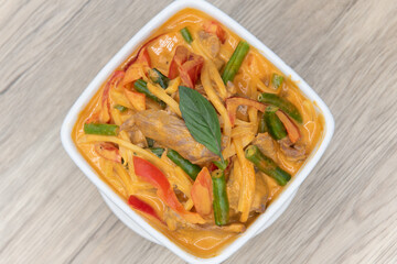 Overhead view of spicy red curry presented perfectly in a bowl served upon a wooden plank table