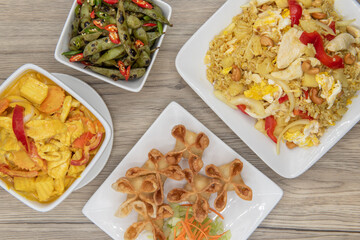 Full feast of spicy Thai food on the wooden table with the featured dish being the star shaped wontons