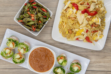Full feast of spicy Thai food on the wooden table with the featured dish being the fresh shriimp rolls