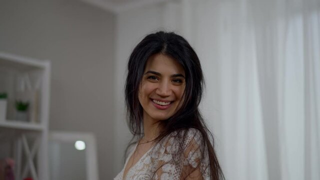 Happy cheerful Middle Eastern bride spinning in elegant white wedding dress laughing. Camera moves up as slim gorgeous confident woman enjoying wedding preparations indoors