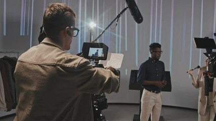 Medium slowmo of professional male video operator setting up camera before filmmaking while his team preparing perfect setup in studio