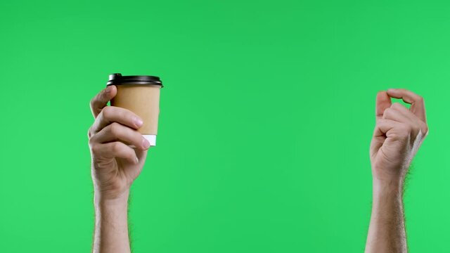 The male hand points with the index finger to the other hand holding a paper cup of coffee and shows the thumb up. Close up of a man's hand on a green screen chroma key background. Slow motion.