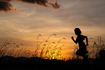 Fototapeta na wymiar Silhouette of child girl running on the meadow at sunset background.