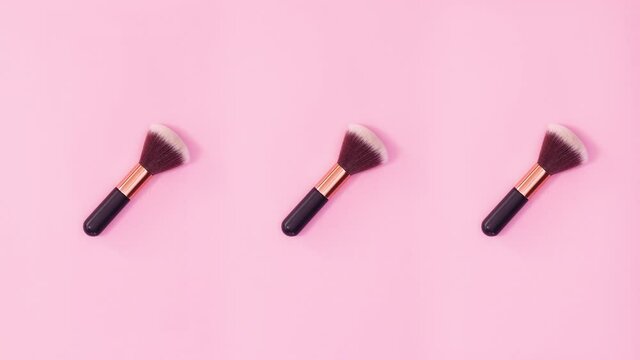 Three make up brushes rotating on bright pink background. Stop motion