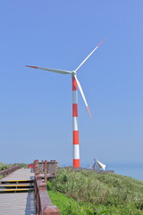 a orange-white wind turbine located by the coast, blue sky as background