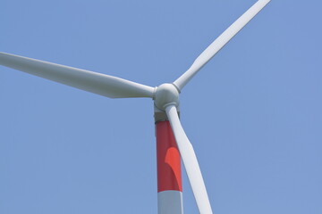 a orange-white wind turbine located by the coast, blue sky as background