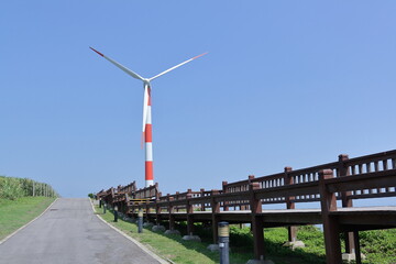 Fototapeta na wymiar a orange-white wind turbine located by the coast, blue sky as background