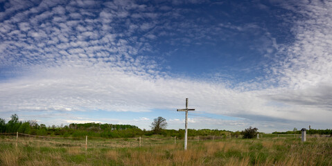 Fototapeta na wymiar Old, dilapidated cemetery with long dead grass and a large white cross. The sky is blue with white clouds. 