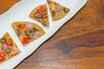 Sliced pieces of  pizza served on a white plate on a wooden table with copy space