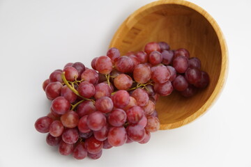 Fresh and ripe red grapes in a wooden bowl, isolated in white background. Bunch of raw and juicy grapevines