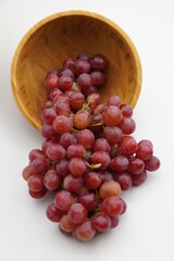 Fresh and ripe red grapes in a wooden bowl, isolated in white background. Bunch of raw and juicy grapevines