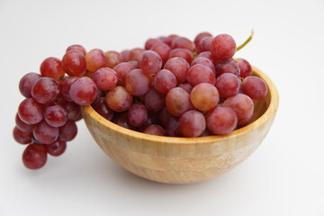Fresh and ripe red grapes in a wooden bowl, isolated in white background. Bunch of raw and juicy grapevines
