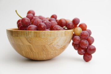 Fresh and ripe red grapes in a wooden bowl, isolated in white background. Bunch of raw and juicy grapevines