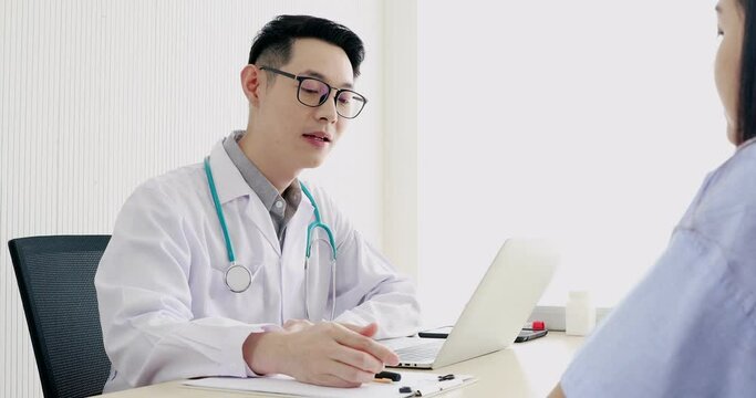Young nice asian doctor with glasses talking and giving his patient some recommendation on the health result by pointing and explaining using his laptop
