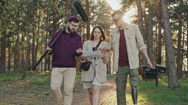 Medium slowmo of professional cameraman with leg prosthesis and his filming crew walking towards camera discussing storyboard for shooting