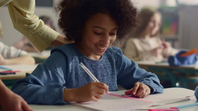 Pupil doing class work at desk. Female teacher helping girl with task of lesson