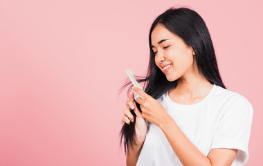 Portrait of Asian beautiful young woman smile combing her hair, happy female long healthy hair with hairbrush brushing hairs, studio shot isolated on pink background