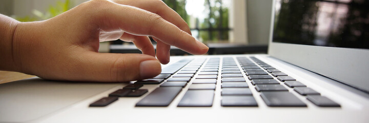 Working by using a laptop computer on wooden table. Hands typing on a keyboard.