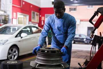 Afro american man working with tire fitting machine at auto car repair service center