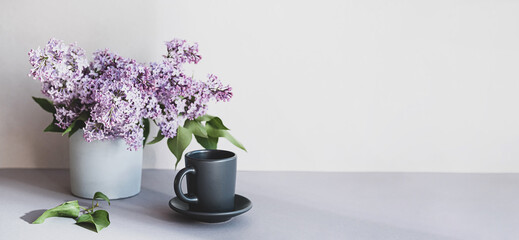 Still life scene with a bouquet of lilacs and a cup of coffee. Minimal, composition with flowers and interesting shadows.