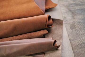 Genuine leather in brown and gray colors. Leather pieces set on a wooden table. Hobby and craft material.Leather goods material.material for the production clothing and footwear