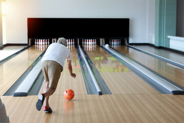 rear view older caucasian men, white beard and white hair in white and blue shirt playing bowling in sport club