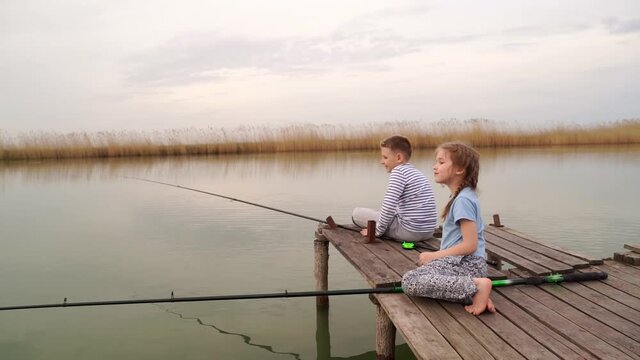 fishermen. little girl and boy fish on a fishing rod sitting on a wooden bridge