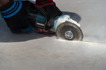 Worker in gloves with a small angle grinder cuts fibre cement, concrete plate in construction site. Builder worker cutting granite slab with using a cut-off saw.