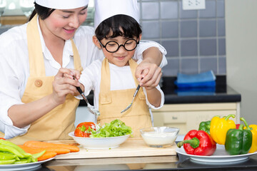 Asian woman young mother with son boy cooking salad food with vegetable holding tomatoes and carrots, bell peppers on plate for happy family cook food enjoyment lifestyle kitchen in home