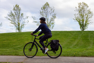 Fototapeta premium Adult Caucasian Woman Riding a Bicycle on a path in a modern city park. Spring Evening. Taken in Hawthorne Rotary Park, Surrey, Vancouver, British Columbia, Canada.