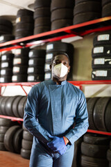 Naklejka na ściany i meble Portrait of a auto mechanic in protective mask in front of car tires