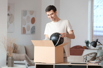 Fototapeta na wymiar Handsome young man unpacking box with globe at home