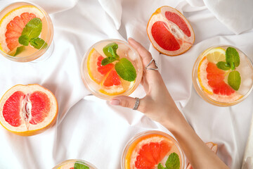 Female hand with glass of tasty grapefruit cocktail on fabric background