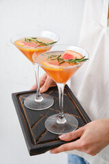 Woman holding board with glasses of tasty grapefruit cocktail on light background, closeup