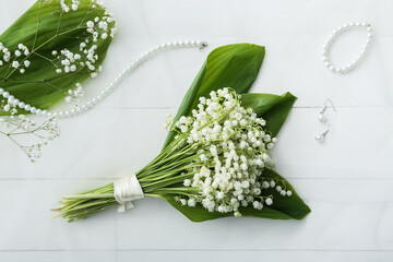 Beautiful lily-of-the-valley flowers and jewelry on light wooden background