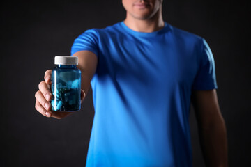 Man with bottle of pills on black background, closeup. Doping concept