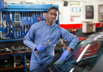 Portrait of confident african male mechanician posing near car on his workplace in workshop