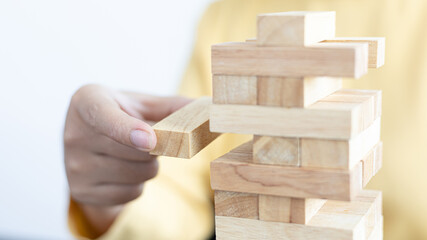 Business growth with wooden blocks concept, Planning to Reduce Investment Risks with Wooden Game Models, hand of a business woman placed a wooden block on a high tower,Management of limited resources.