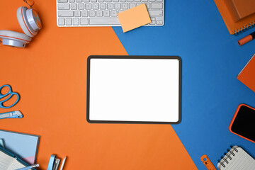 Mock up digital tablet .surrounded by office supplies on two tone blue and orange background.