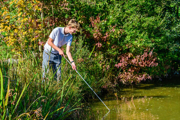 Junger Golfer fischt einen Ball aus dem Teich