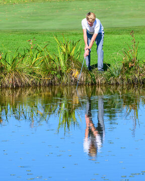 Junger Golfer fischt einen Ball aus dem Teich