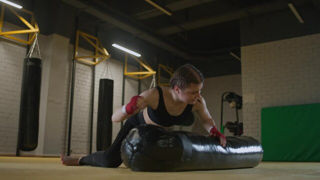 Aggressive female fighter trains his punches, beats a punching bag while lying on the floor, training day in the boxing gym, strength fit body, the girl strikes fast.