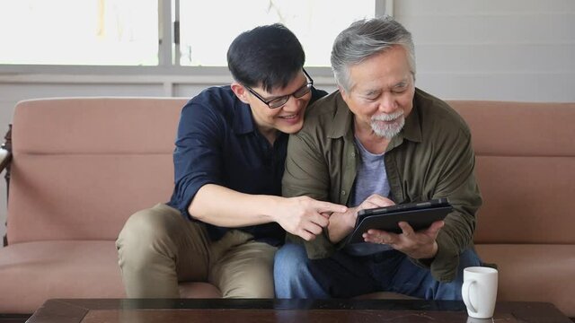 Senior Asian man in retirement age and his son who teach him to use digital tablet to looking at photo of product available online
