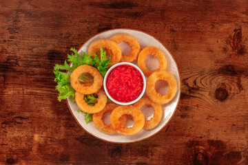 Squid rings. Deep fried calamari rings with lettuce and ketchup, shot from the top on a dark rustic wooden background