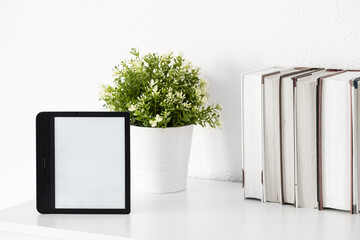 E-book  on white  book shelf with green plant. Modern reader device mocke up. Copy space