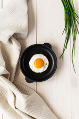 Fried eggs in a cast iron skillet with green onions and a linen towel. Vertical orientation, top view.