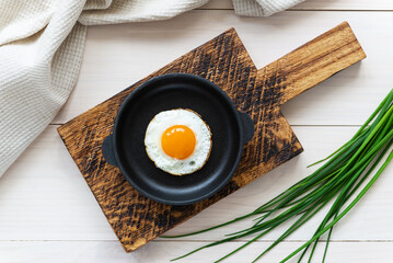 Fried eggs in a cast iron skillet on a wooden board with green onions and a linen towel. Horizontal...